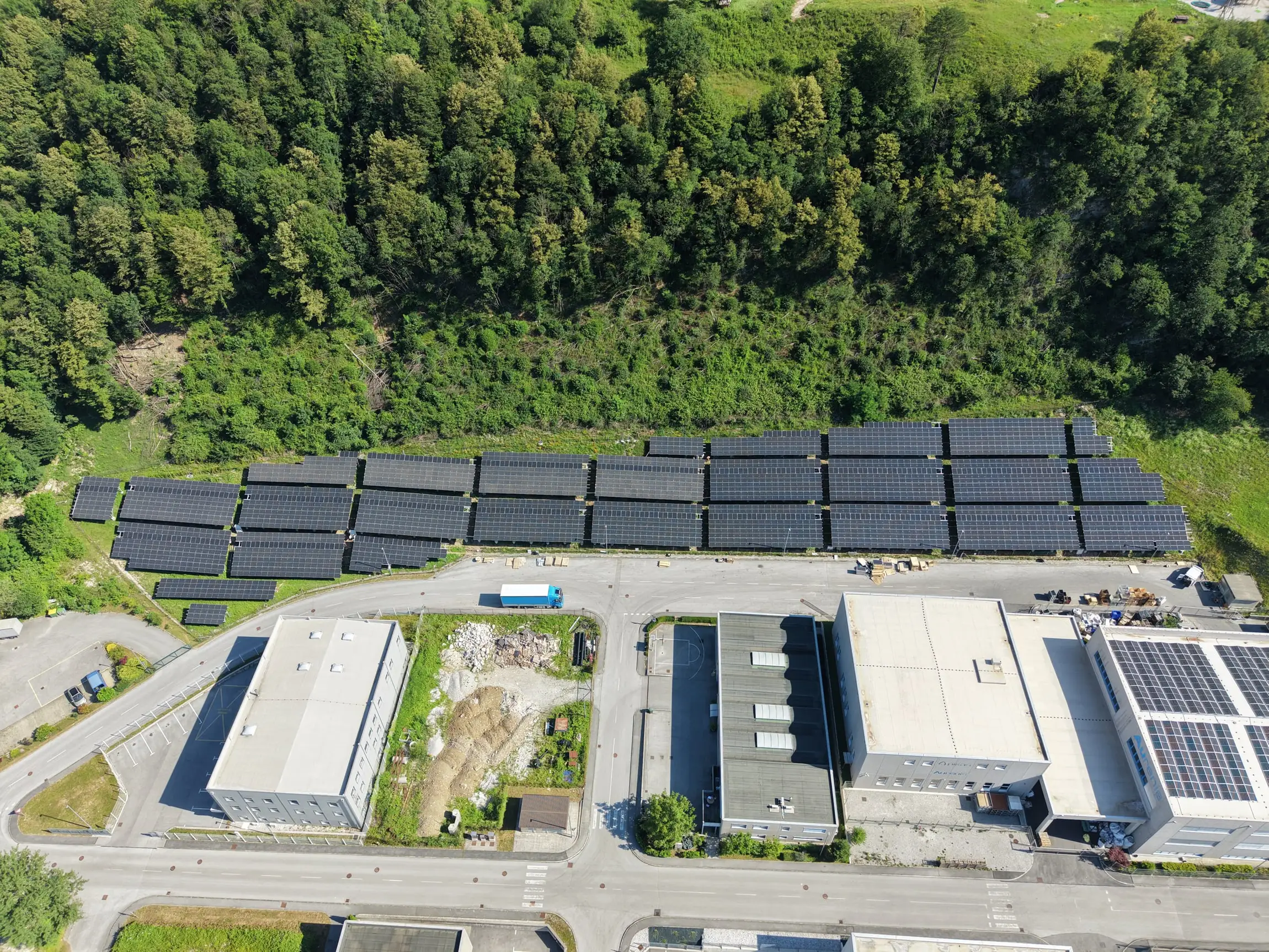Zračni posnetek dolgih vrst talno postavljenih sončnih modulov ob industrijskih objektih